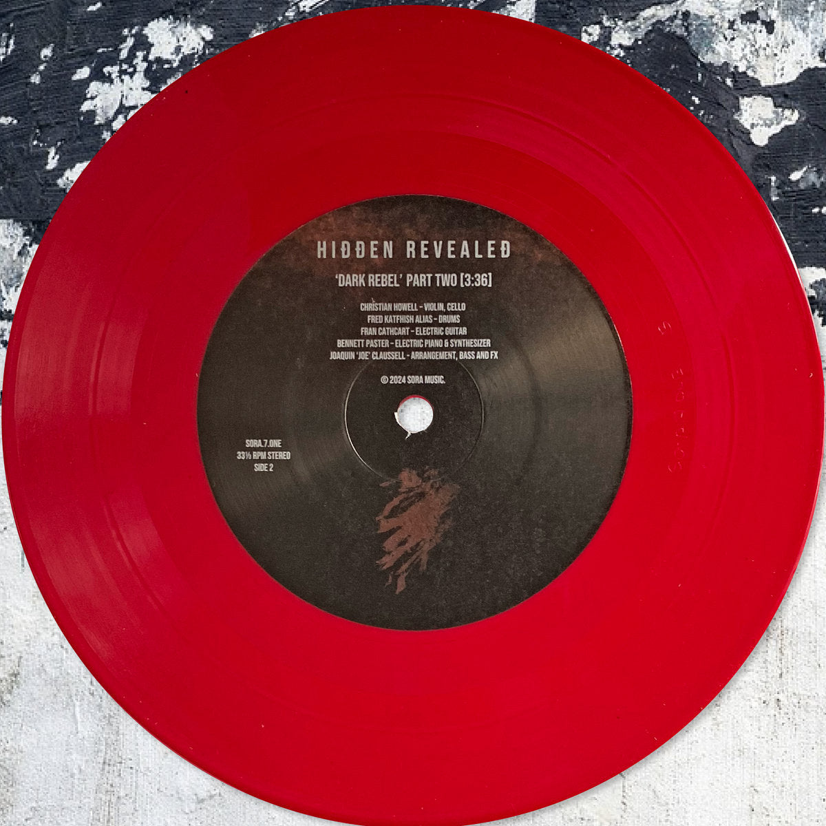 Vinilo rojo traslúcido Hidden Revealed – Dark Rebel en edición limitada 7" de SORA; enfocado en el lado B con etiqueta central legible sobre fondo texturizado.