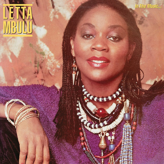 Portada delantera del vinilo Letta Mbulu – In The Music... The Village Never Ends de Be With Records. Texto impreso: “In The Music...” y nombre de la artista en tipografía amarilla.