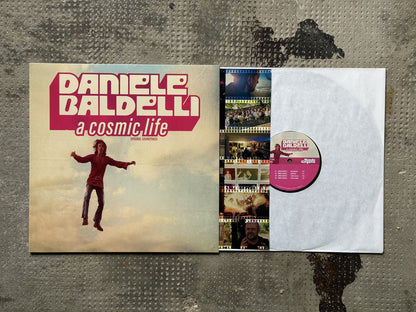 Funda e interior del vinilo Daniele Baldelli – A Cosmic Life (Original Soundtrack), LP de Mondo Groove con insert fotográfico y etiqueta central rosa con pistas visibles.