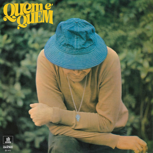 Portada del vinilo João Donato – Quem É Quem con el artista agachado y sombrero azul frente a un fondo vegetal.