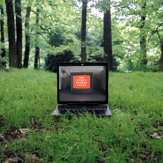 Portada del vinilo The Other People Place – Lifestyles Of The Laptop Café con laptop en medio del bosque mostrando una pantalla con el texto del artista.